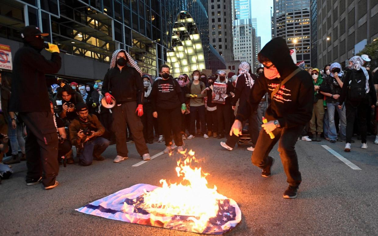 A protestor burning a US-Israel flag, as many others watch on