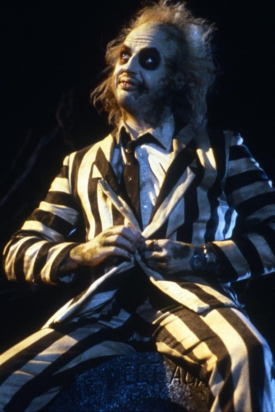 Beetlejuice character sitting on a tombstone in a striped suit