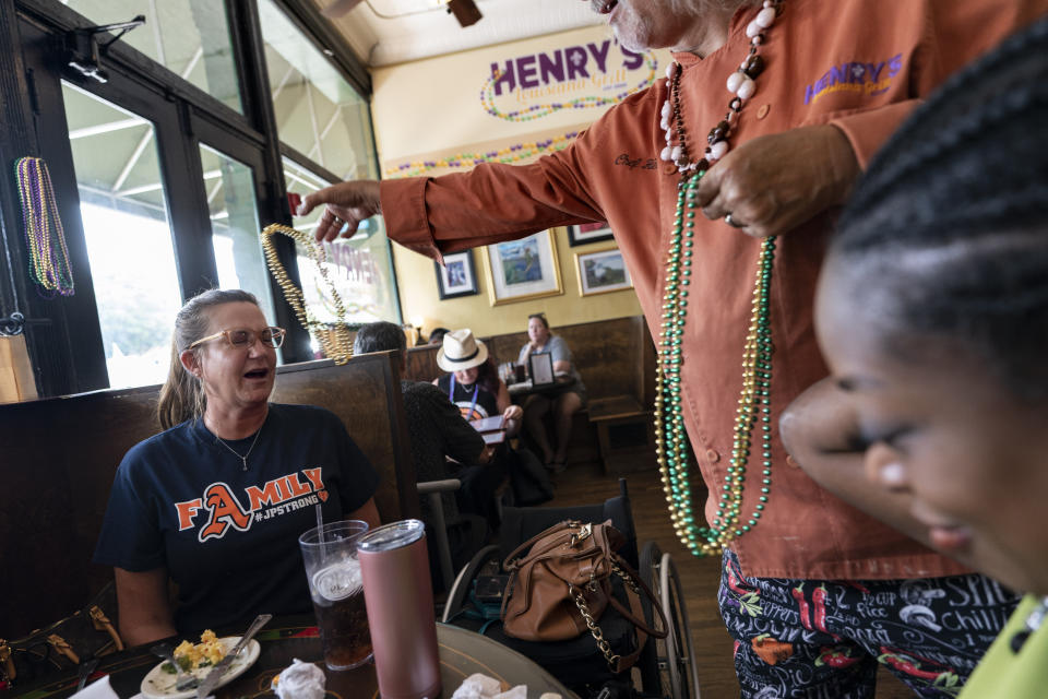 Henry Chandler tosses beads over Janet Paulsen’s head, left, as she enjoys lunch at his restaurant, Henry’s Louisiana Grill, with TaNesha McAuley, right, of the Cobb Family Advocacy Center, in Acworth, Ga., Tuesday, Aug. 8, 2023. The center helps victims of domestic violence, sexual assault and child abuse. (AP Photo/David Goldman)