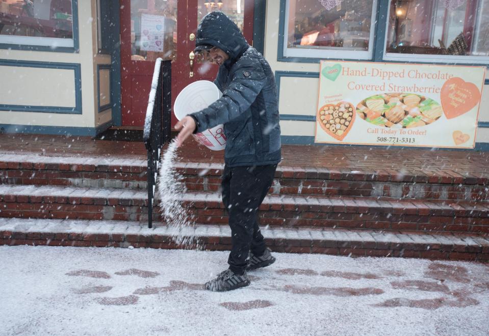 Mavae Valdo sends out a stream of salt on Tuesday in front of Kandy Korner in Hyannis to keep the sidewalk clear for Valentine's Day shoppers as a heavy wet snow fell most of the day.