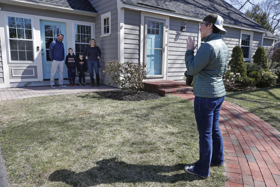 In this Friday, March 27, 2020 photo, photographer Jen Bauer arranges the Bates family for a portrait as part of the Front Steps Project in North Andover, Mass. With many families housebound during the coronavirus pandemic, photographers are raising money for local charities by offering portraits from a distance. (AP Photo/Elise Amendola)