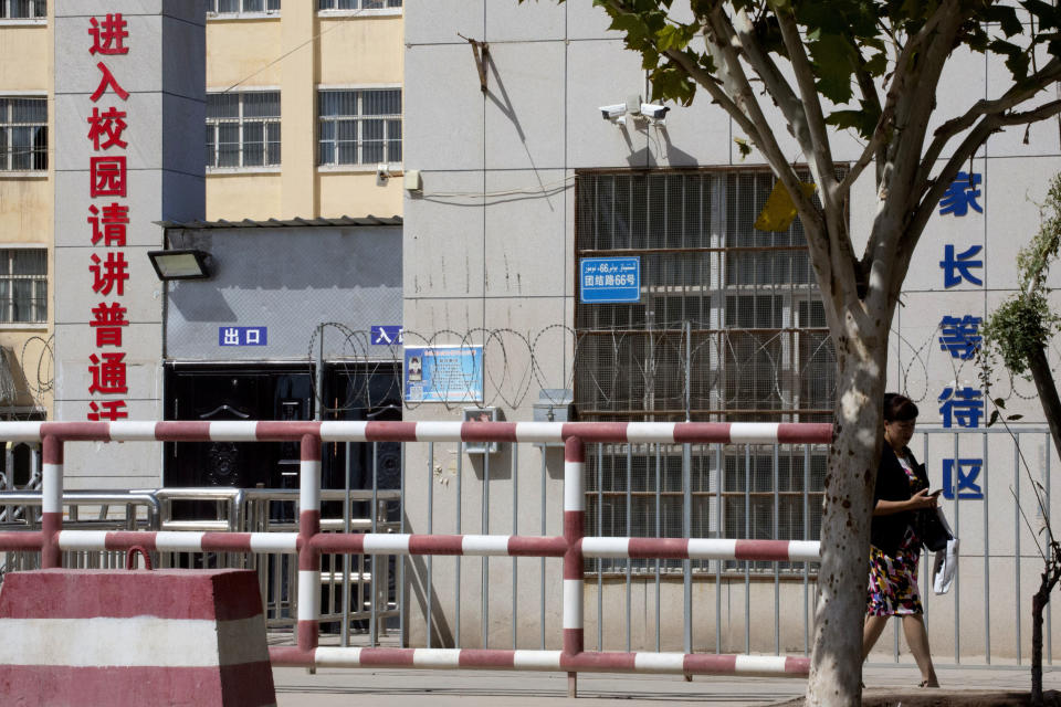 In this Aug. 31, 2018, photo, a woman walks past the entrance to the No. 4 High School also known as the Peyzawat Bilingual High School with signs which read "Entering School Grounds, Please speak Mandarin," left, and "Parents Waiting Zone" in Peyzawat, western China's Xinjiang region. Uighurs fear the Chinese government's expansion of compulsory Mandarin-intensive classes and boarding schools away from home will gradually erode their children's Central Asian ethnic identity and Islamic beliefs. (AP Photo/Ng Han Guan)