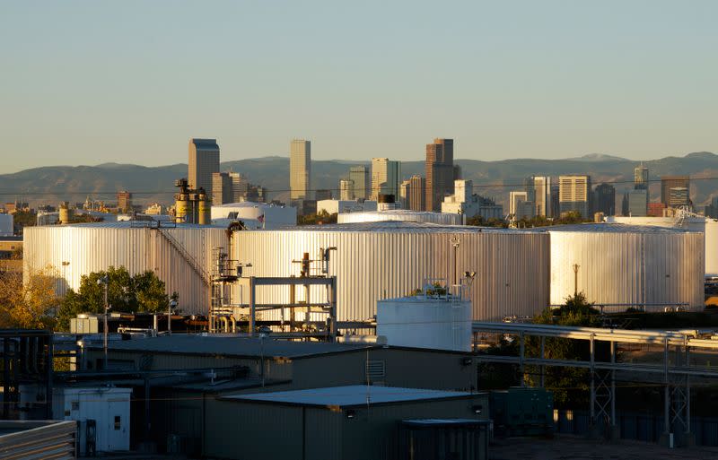 Oil storage tanks are seen at sunrise with the Rocky Mountains and the Denver downtown skyline in the background