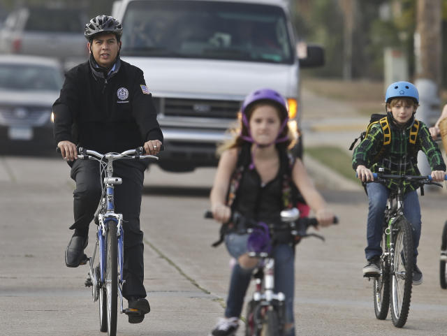 In a Thursday, Jan. 30, 2014 photo, San Diego Mayoral candidate David Alvarez, right, rides through traffic with children and parents headed to school, in San Diego. Alvarez finished second in a first round of voting by winning south of the freeway in predominantly Latino areas. Republican Councilman Kevin Faulconer easily topped a field of 11 candidates in a first round of voting by dominating in wealthier neighborhoods north of the freeway. (AP Photo/Lenny Ignelzi)