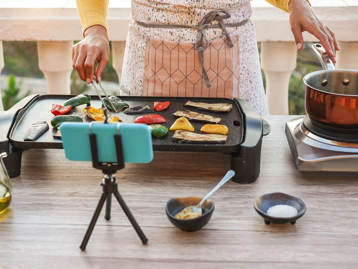 Young woman chef cooking outdoor while streaming online for webinar masterclass lesson at home - Girl making videos preparing vegetarian meal on her patio terrace - Food concept - Focus on hands