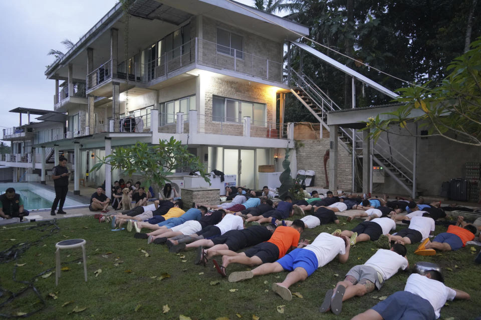 In this photo released by the Directorate General of Immigration of Indonesia's Justice and Human Rights Ministry (Ditjen Imigrasi), foreign nationals from China, Taiwan and Malaysia who are detained on allegations of conducting cybercrime and visa violations are lined up on the ground following a raid on a villa in Tabanan, Bali, Indonesia, Wednesday, June 26, 2024. (Ditjen Imigrasi via AP)