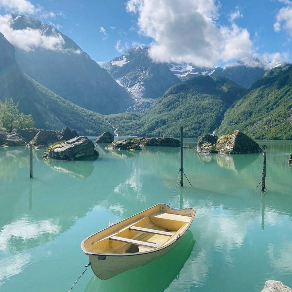 a row boat floats atop blue-green waters in Mauranger, with mountrains in the background