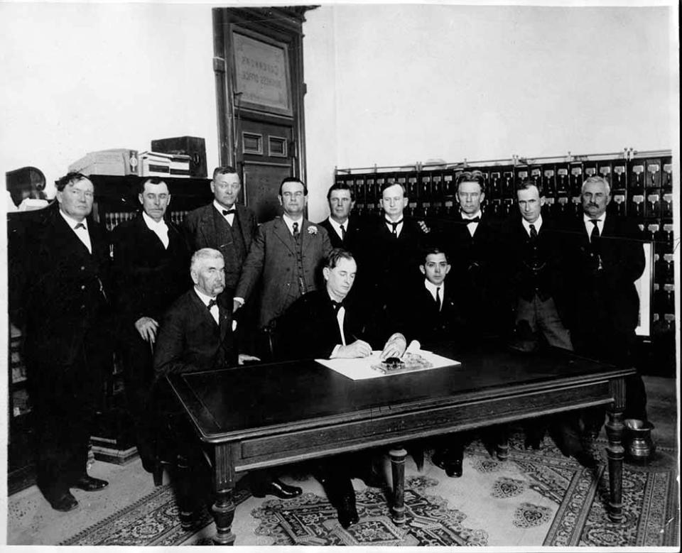 Gov. Pat Neff signs Senate Bill 103 into law creating Texas Technological College. William Bledsoe is standing directly behind the governor.