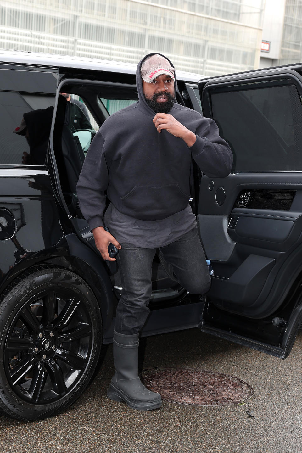 Kanye West in black hoodie, black pants, and boots