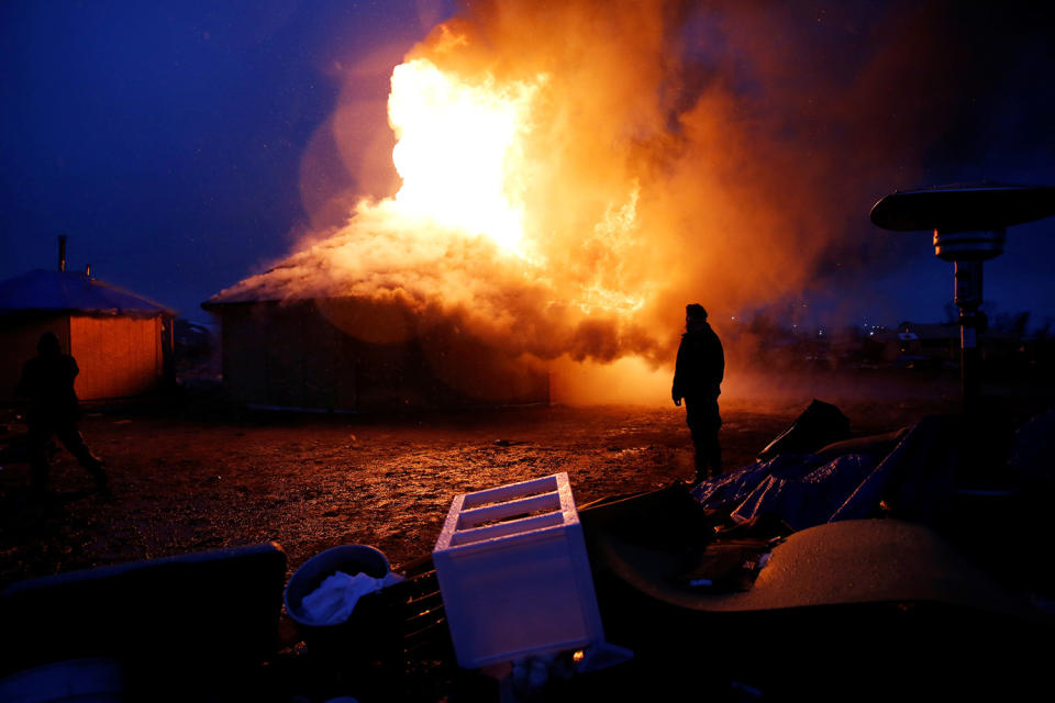 <p>Chanse Zavalla, 26, from California, watches a building burn after it was torched by protesters preparing to evacuate the main opposition camp against the Dakota Access oil pipeline, near Cannon Ball, N.D., Feb. 22, 2017. (Photo: Terray Sylvester/Reuters) </p>