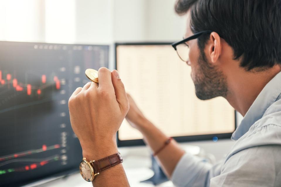 A person who watches stock price trends on a computer and holds coins.