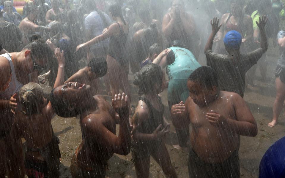 Children and adults rinse the mud off during Mud Day at the Nankin Mills Park, Tuesday, July 9, 2019, in Westland, Mich. The annual day is for kids 12 years old and younger. While parents might be welcome, this isn't an event meant for teens or adults. It's all about the kids having some good, unclean fun during their summer break and is sponsored by the Wayne County Parks. (AP Photo/Carlos Osorio)