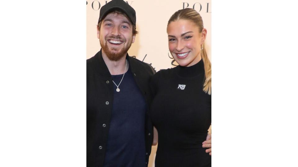 Sam Thompson and Zara McDermott smiles as they pose in front of branding for fashion event