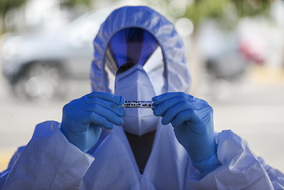 A healthcare worker holds a sample of a nasal swab after testing a passenger at a drive-thru new coronavirus testing site outside a supermarket in Santiago, Chile, Saturday, June 27, 2020. (AP Photo/Esteban Felix)