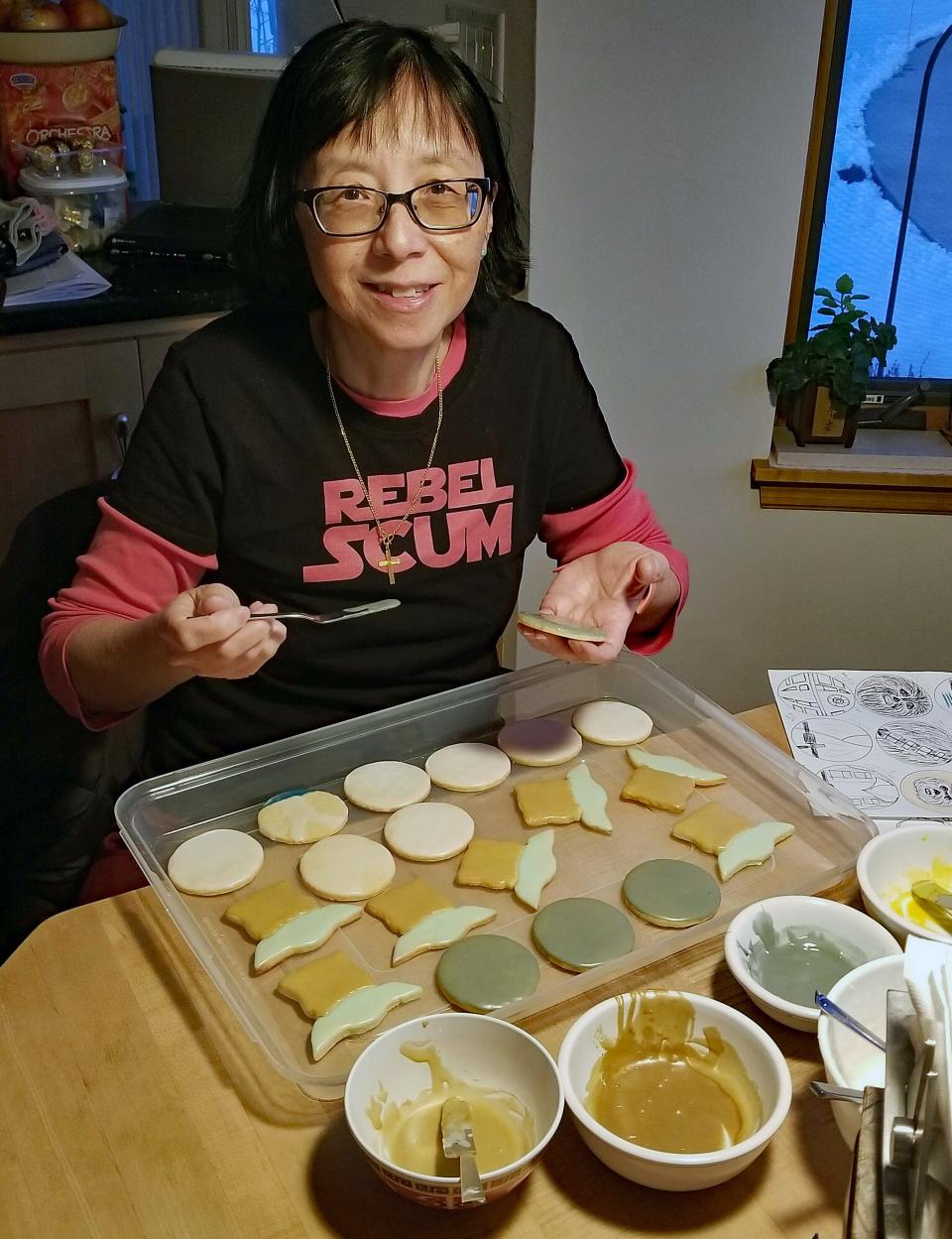 Glazing a few dozen cookies can take several hours. Here, Mabel glazes “Mandalorian” and “Star Wars” themed cookies for the first birthday of her grand-nephew, Henry.