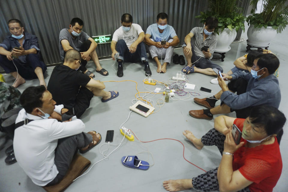 Migrant workers share power source in an exhibition hall after being evacuated from their workplaces in Hangzhou in eastern China's Zhejiang province Sunday, July 25, 2021. A typhoon blew heavy rain across the Shanghai region Monday, leaving roads and low-lying areas waterlogged and felling billboards and signs on its second landfall in eastern China. (Chinatopix via AP)