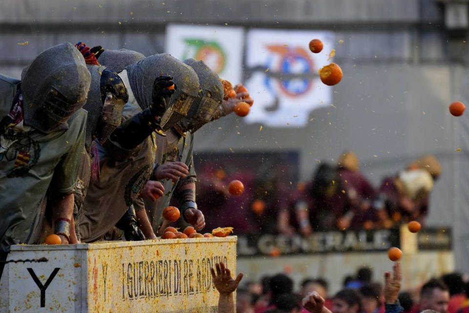 People wearing protection helmets and costumes pelt each other with oranges during the 'Battle of the Oranges" part of Carnival celebrations in the northern Italian Piedmont town of Ivrea, Italy, Tuesday, Feb. 13, 2024. (AP Photo/Antonio Calanni)