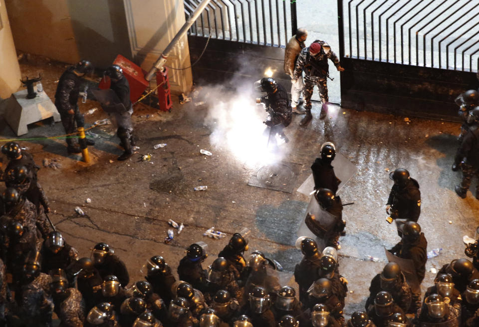 A riot police officer kicks a firecracker that was fired by an anti-government protesters, who are protesting outside a police headquarters demanding the release of those taken into custody the night before, outside a police headquarter, in Beirut, Lebanon, Wednesday, Jan. 15, 2020. Lebanese security forces arrested 59 people, the police said Wednesday, following clashes overnight outside the central bank as angry protesters vented their fury against the country's ruling elite and the worsening financial crisis. (AP Photo/Hussein Malla)