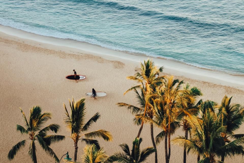 People walking down the beach in Hawaii with surfboards