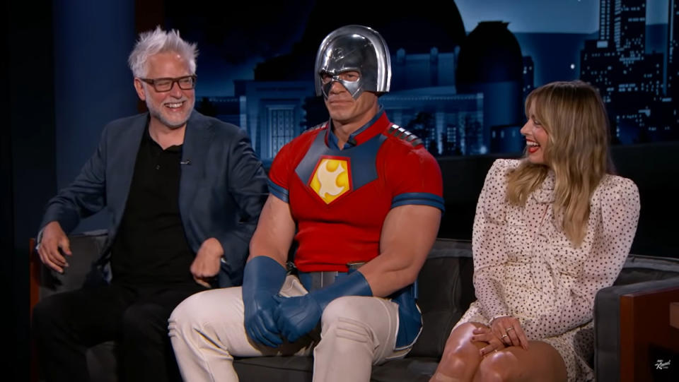 James Gunn, John Cena in a Peacemaker costume, and Margot Robbie sit next to each other