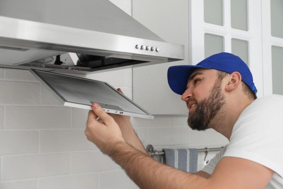 A man in a blue cap adds a component to a new range hood.