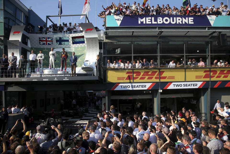 In this March 17, 2019, file photo, the award ceremony for the Australian Formula 1 Grand Prix is watched by team supporters while Mercedes driver Valtteri Bottas of Finland, teammate Lewis Hamilton of Britain and Red Bull driver Max Verstappen of the Netherlands stand on the podium in Melbourne, Australia. The start of the 2021 Formula One season has been delayed after the Australian Grand Prix was postponed because of the coronavirus pandemic. The Australian race in Melbourne has been rescheduled from March 21 to November 21. (AP Photo/Rick Rycroft, File)