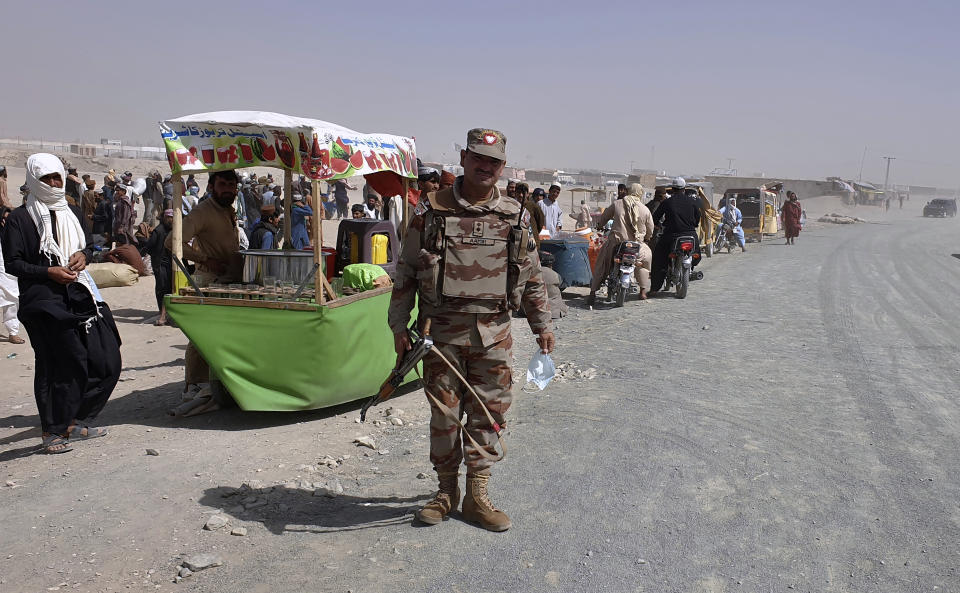 A Pakistan army soldier stands guard while stranded people gather and wait to open the border which was closed by authorities, in Chaman, Pakistan, Saturday, Aug. 7, 2021. Chaman border crossing is one of busiest border crossings between Pakistan and Afghanistan. Thousands of Afghans and Pakistanis cross daily and a steady stream of trucks passes through, taking goods to land-locked Afghanistan from the Arabian Sea port city of Karachi in Pakistan. (AP Photo/Tariq Achakzai)