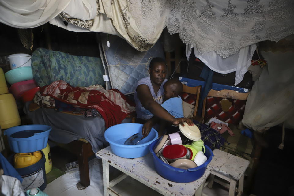 Jacinter Awino, 33, holds her son as she cleans utensils in the Kibera slum of the capital Nairobi, Kenya, Tuesday, May 28, 2024. Jacinter shares a small tin house with her husband and four children. The 33-year-old housewife and her mason husband are unable to raise the $3,800 purchase price for a one-room government house. Their tin one was constructed for $380 and lacks a toilet and running water. (AP Photo/Andrew Kasuku)