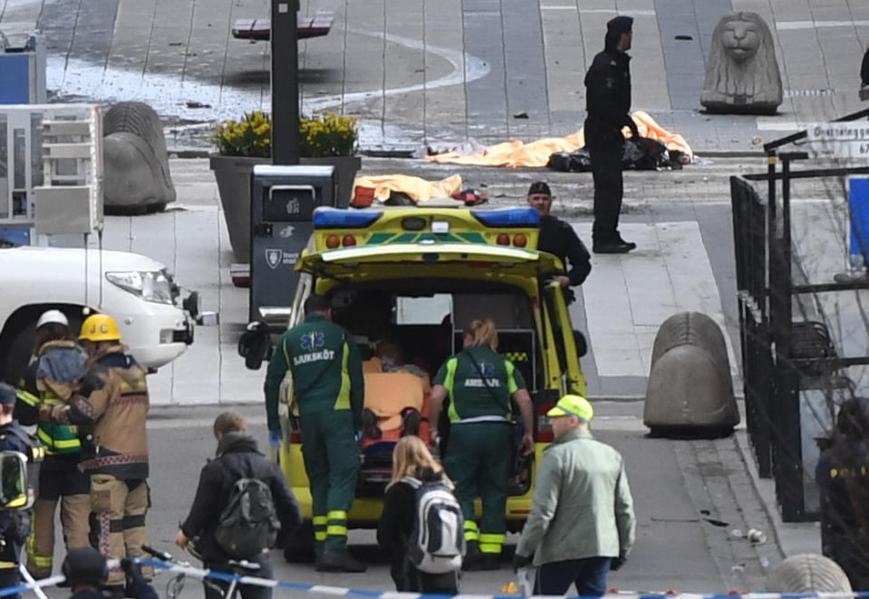 Empleados de emergencias atienen a una persona en una ambulancia (al centro) después de que un camión chocó contra una tienda departamental en el centro de Estocolmo, el viernes 7 de abril de 2017. (Fredrik Sandberg/TT News Agency vía AP)