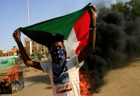 A protester carries a Sudanese national flag as he burns tyres during a demonstration against a report of the Attorney-General on the dissolution of the sit-in protest in Khartoum