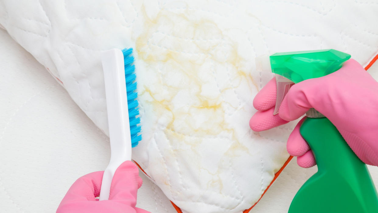  A person wearing pink disposable gloves cleans yellow stains from a white pillow. 