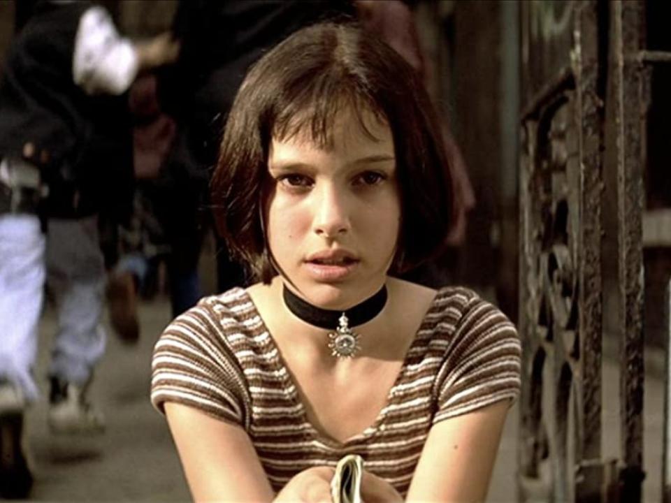 A young Natalie with bangs, a choker necklace, and striped shirt sitting on a curb.