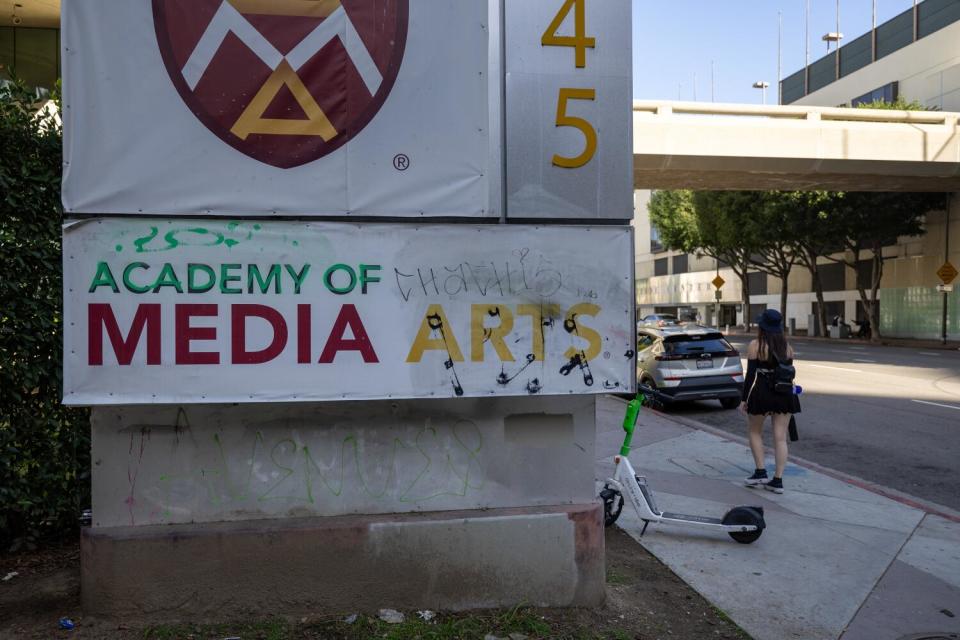 Graffiti on a school sign, trash and an abandoned scooter in front of the Academy of Media Arts school.