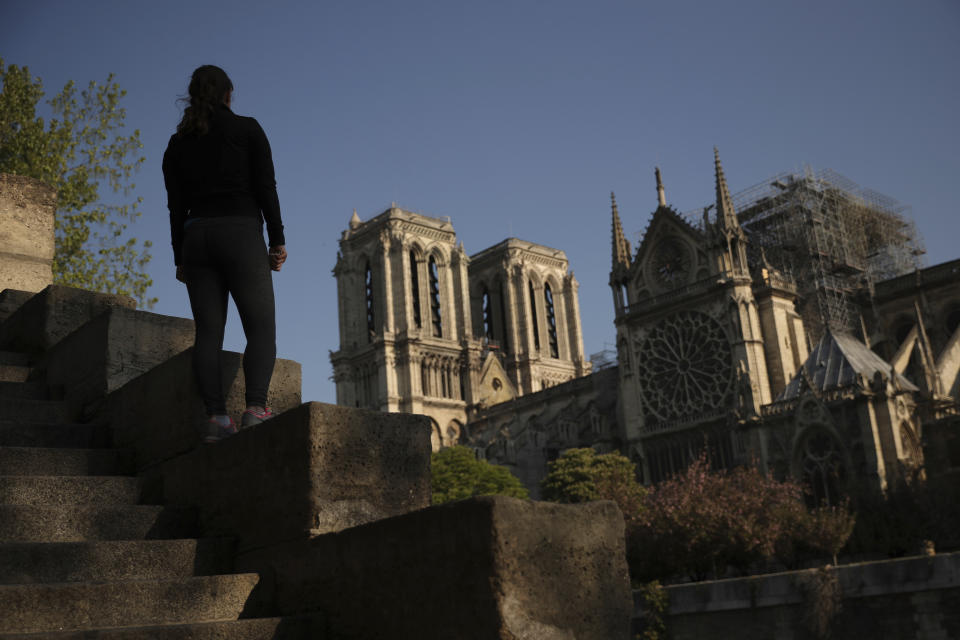 A woman stands on steps near the Notre Dame Cathedral in Paris, Saturday, April 20, 2019. Rebuilding Notre Dame, the 800-year-old Paris cathedral devastated by fire this week, will cost billions of dollars as architects, historians and artisans work to preserve the medieval landmark. (AP Photo/Francisco Seco)