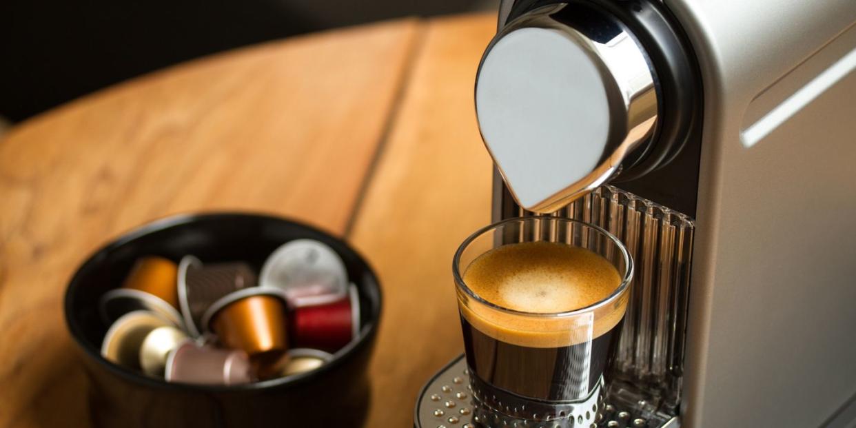 copenhagen, denmark   july 8, 2014 freshly brewed espresso in glass standing on silver nespresso coffe machine blurred background with nespresso capsules in black bowl