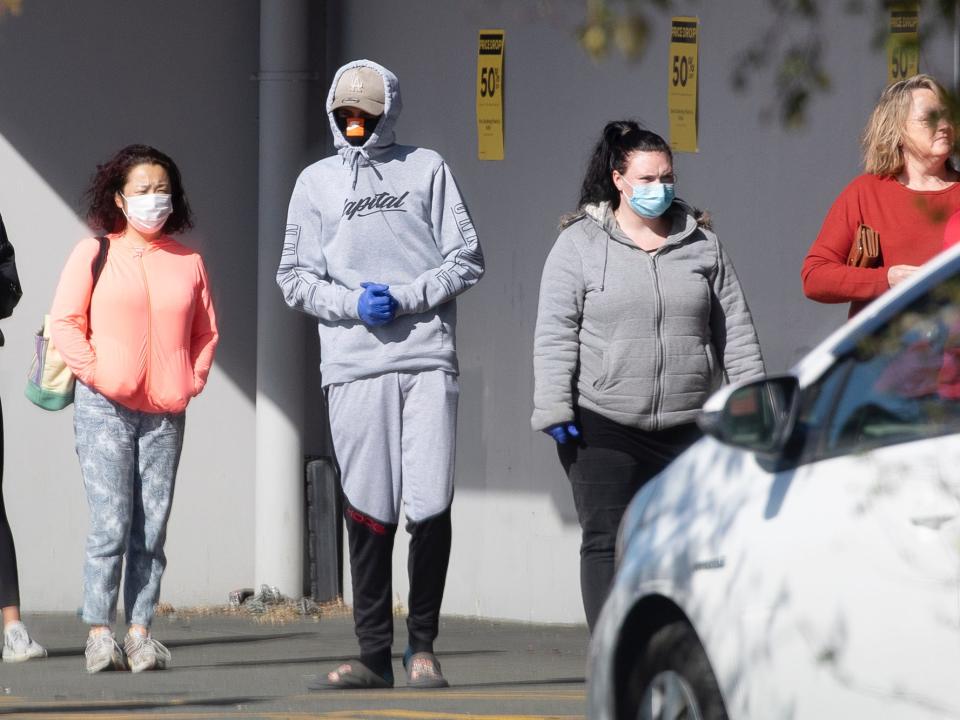 People wearing face masks, stand in a queue to enter a shop in Christchurch, New Zealand, on March 25, 2020.