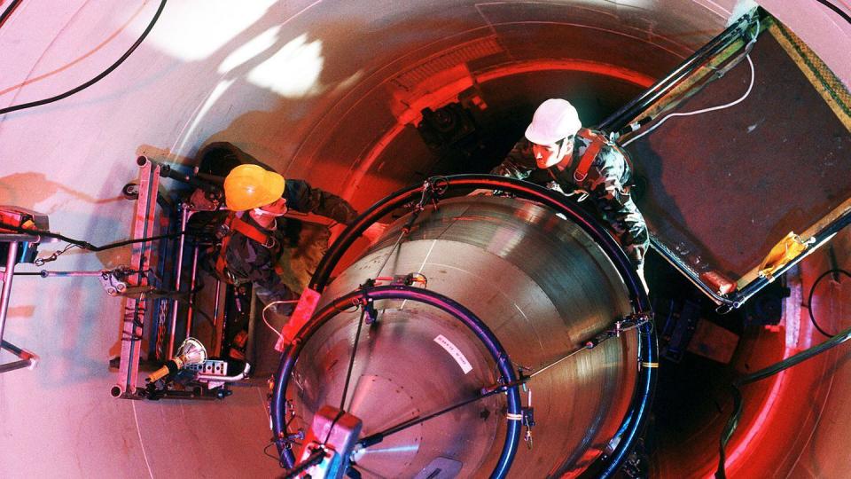 In this September 1990 photo, Senior Airman Scott Fowler (top) and Senior Airman Paul Gallegos, maintenance personnel with the 321st Strategic Missile Wing, guide the re-entry system for an LGM-30 Minuteman III missile onto a missile guidance set. (Air Force)