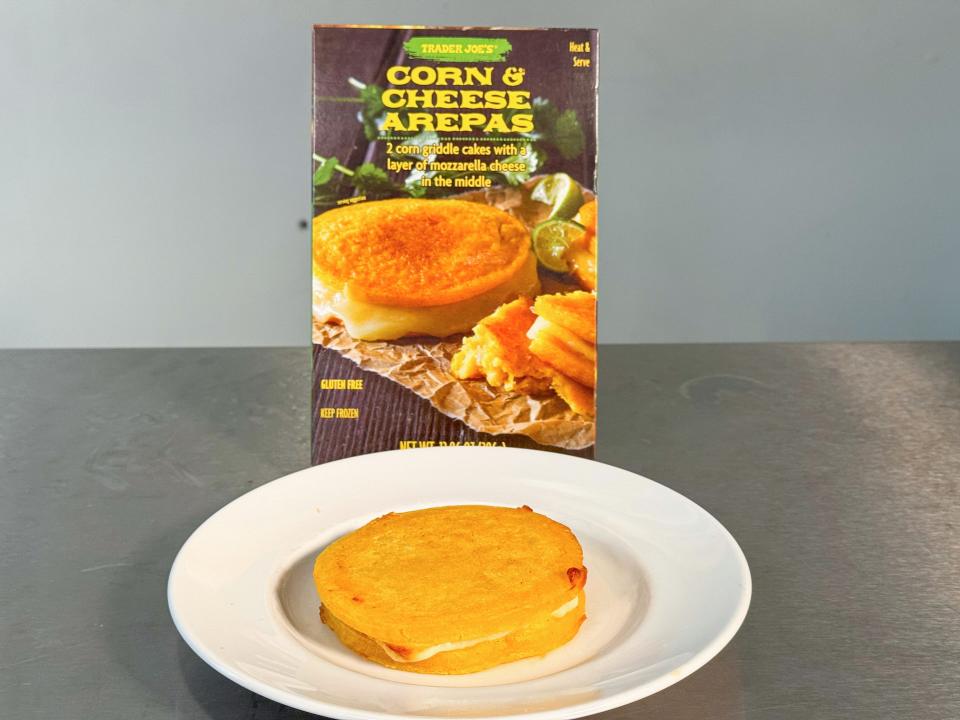 A plate with a corn-and-cheese arepa in front of a gray box of arepas