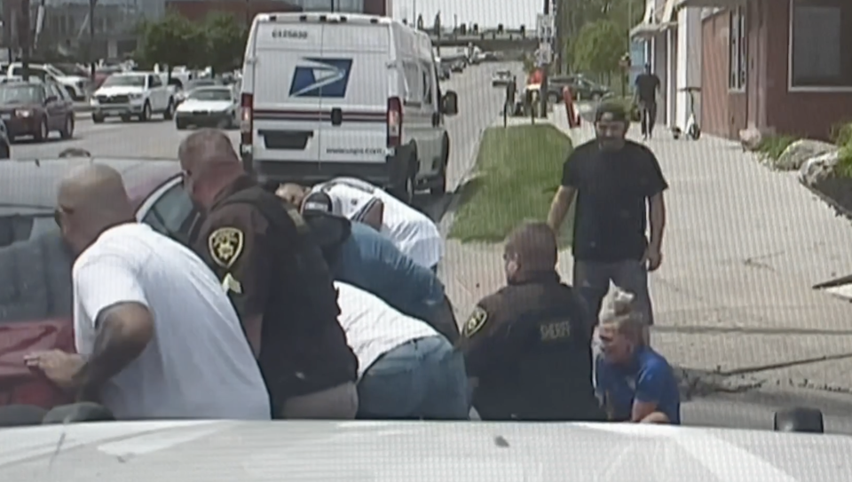 Multiple bystanders including Sean Graham and his neighbor help lift the car pinning down Andrew Busch. Lt. Timothy Owens is helping pull Busch from underneath it. (Screenshot of dash cam footage via Douglas County Sheriff's Office)