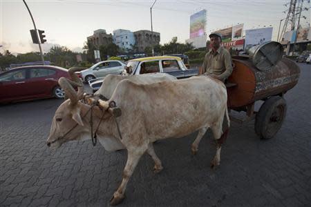 A man sits on his bullock-pulled oil delivery wagon as traffic passes on a highway in Mumbai in this May 4, 2011 file photo. REUTERS/Vivek Prakash/Files
