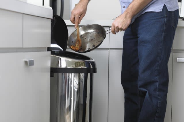 Man Scraping Burnt Food into a Bin in a Kitchen