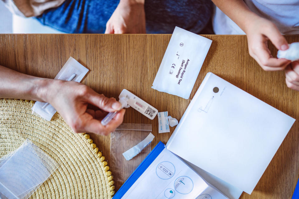 Directly above view of mom squeezing the sample liquid on a test strip while carrying out a Covid-19 rapid self test for her kid at home. / Credit: tangmingtung@gmail.com / Getty Images