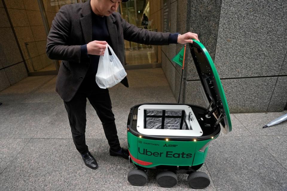優食日本分公司3月6日開始在東京限定區域試辦機器人外送服務，圖為3月5日的街頭實演中，一名上班族打開箱子取餐。美聯社