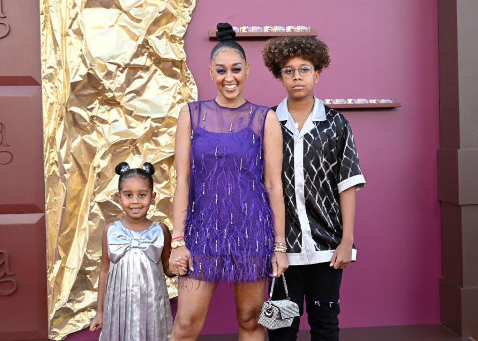 Tia in a sheer, fringed dress with her two children by her side at an event