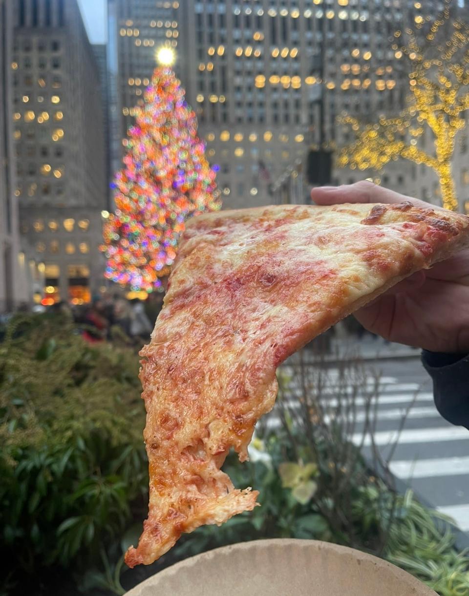A slice of plain pizza from 2 Bro's Pizza in New York City, in front of the Rockefeller Center Christmas tree.