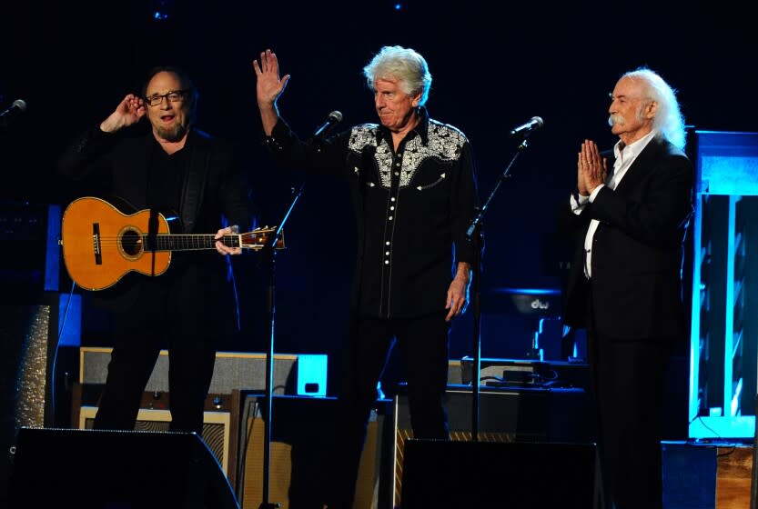 Stephen Stills holding a guitar, left, Graham Nash waving and David Crosby touching his hands together