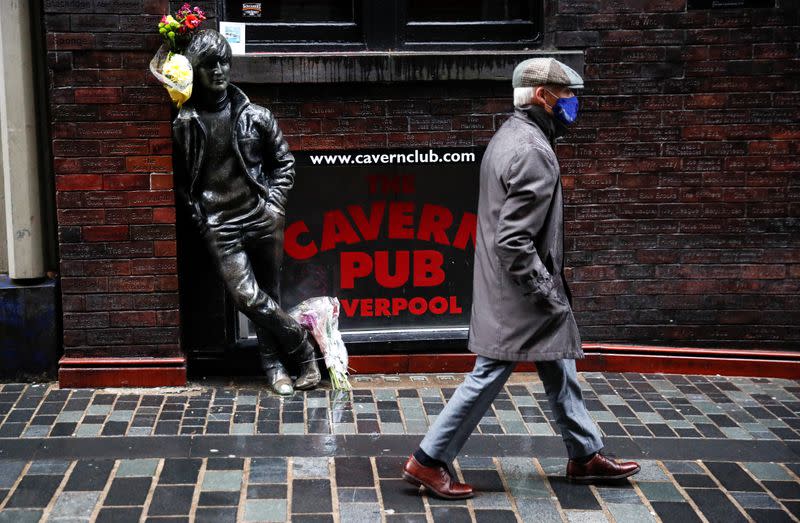 A man wearing a face mask walks past John Lennon statue in Liverpool