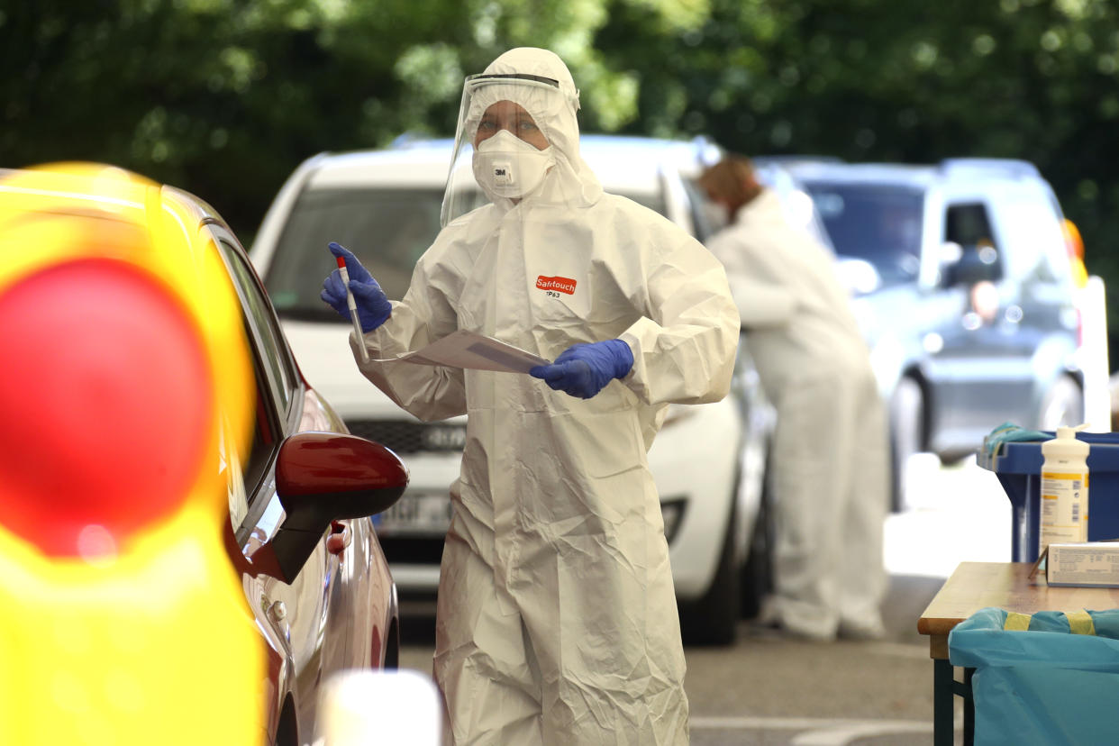 Health workers collect samples at a makeshift COVID-19 testing station in Mamming, Germany, Tuesday, July 28, 2020. After a local coronavirus outbreak on the cucumber farm premises, state authorities have quarantined the entire farm and its workers. (AP Photo/Matthias Schrader)