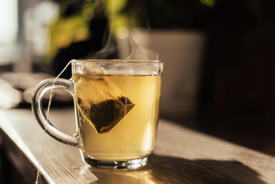 putting tea bag into glass cup full of hot water