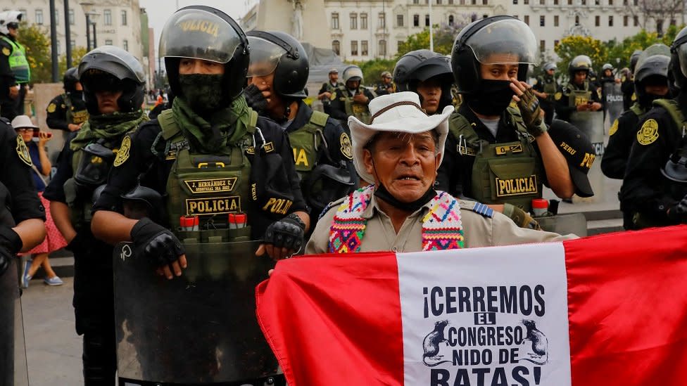 Un indígena con una bandera que pide la renuncia del Congreso.